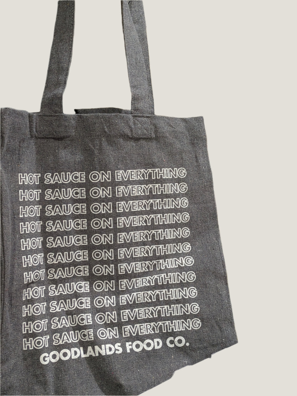 Gray tote bag with 'Hot Sauce on Everything' text in a store setting with hot sauce bottles.